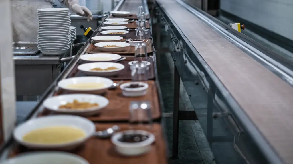 Bandejas con platos y vasos en una línea de cocina industrial de un comedor hostelero, preparadas para el servicio.