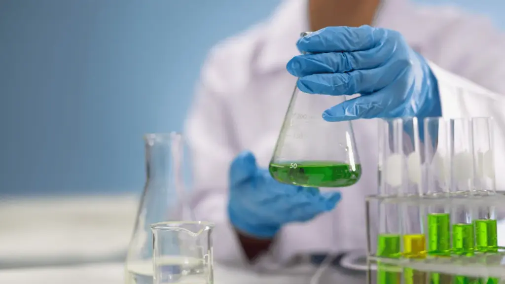Científico manipulando una muestra verde en un matraz durante el proceso de investigación y desarrollo de biocombustibles avanzados a partir de aceites usados.